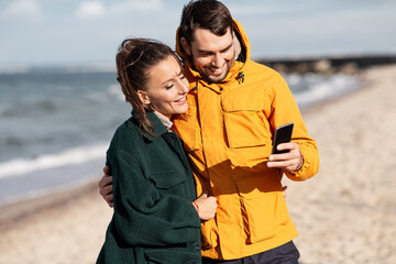 Poster - technology, relationships and people concept - happy couple with smartphone on autumn beach