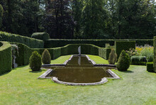 Park With Hedges Of Conifers And Boxwood With A Pond With A Statue Behind It