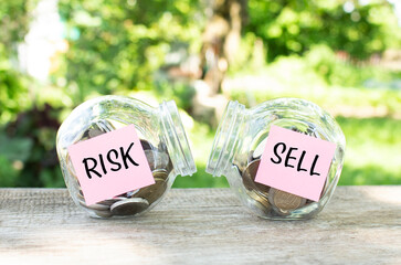 Glass jars with coins and the inscriptions RISK and SELL stand on a wooden table. Investment budget.