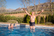 © ADDICTIVE STOCK - Shirtless excited man jumping in pool with raised arms