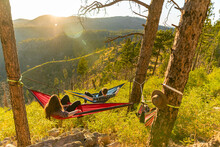 Female In A Red And A Man In A Blue Hammock Enjoying The Sunset On The Slope Of A Mountain