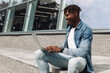 © Shopping King Louie - black african american man typing on a laptop on the street in front of a glass building sitting, online work away