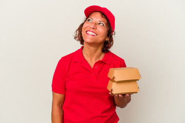 Middle age delivery woman taking burguers isolated on white background dreaming of achieving goals and purposes