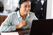 © lordn - Young Asian woman attending online foreign language classes. Sitting in front of laptop computer with headphones listening course and taking notes.