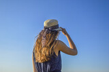 Fototapeta  - Blue sky and a girl with a dress and a hat standing backwards