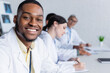 © LIGHTFIELD STUDIOS - young african american doctor smiling at camera near colleagues working on blurred background