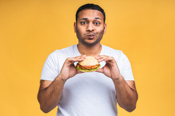 Young african american indian black man eating hamburger isolated over yellow background. Diet concept.