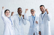 excited multicultural doctors in white coats with name tags showing rejoice gesture