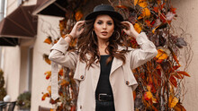 Fashionable portrait of a beautiful young woman with sexy lips in stylish vintage clothes with a hat and a gray coat walking in the city with yellow autumn foliage