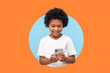 © khosrork - Happy excited boy with curly hair reading message on smartphone and smiling, satisfied with children mobile application, using cellphone. indoor shot isolated in a round hole on orange background