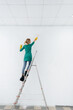 © Andrii - A young girl on a stepladder paints a white wall with a roller. Repair of the interior.