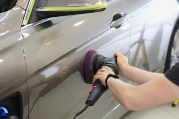 Wall Mural - Master repairman polishing car door using special machine in workshop closeup