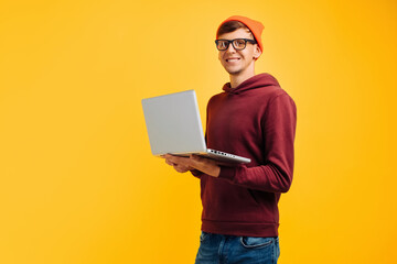 young handsome guy with typing on a laptop, in an orange hat with glasses and a red sweater, on a ye