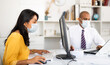 © JackF - Focused hispanic businesswoman in disposable face mask working on computer in office. Necessary precautions during COVID 19 pandemic.