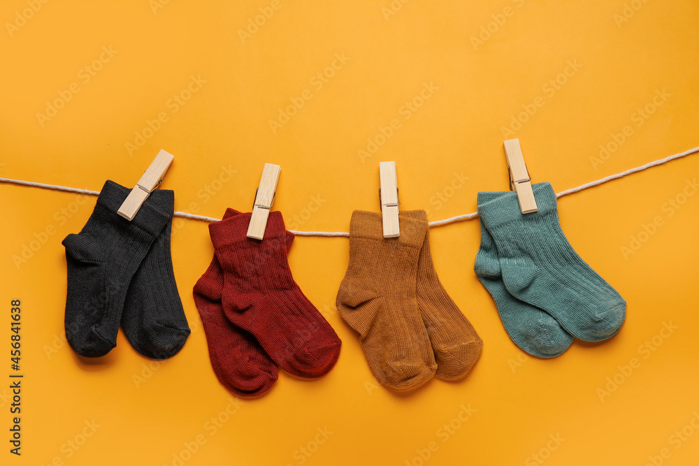 Different baby socks hanging on rope against color background