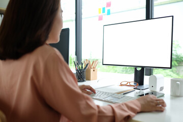 Rear view businesswoman working with computer while sitting in modern workplace.