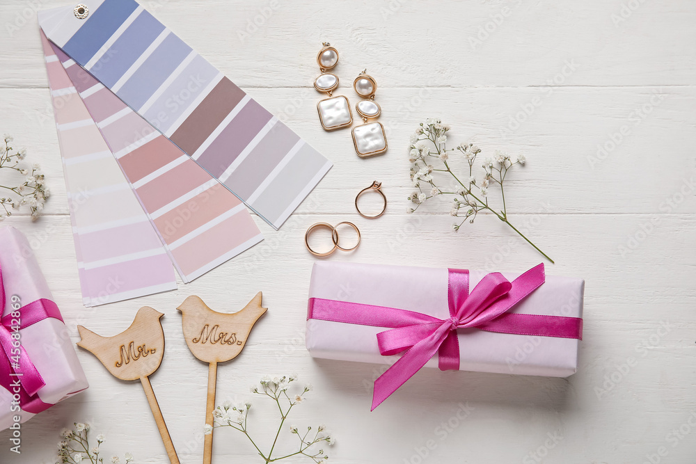 Wedding rings, stylish accessories, color samples and gift boxes on white wooden background