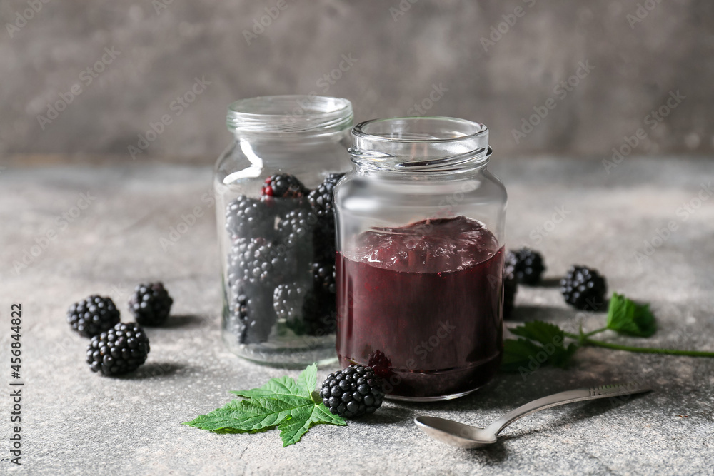 Jars with tasty blackberry jam and berries on grunge background