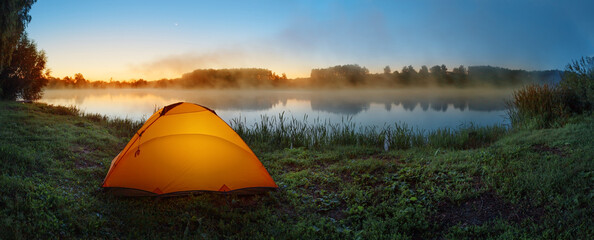 Wall Mural - Orange tent on shore of misty lake at sunrise