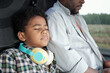 © pressmaster - Black boy with curly hair leaning on shoulder of father while napping in bus