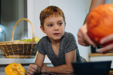 Caucasian cute 6 year old boy looking at his dad carving pumpkin to make traditional Jack lantern.