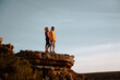 © StratfordProductions - Young couple holding hands looking away standing at peak of cliff after successful hike