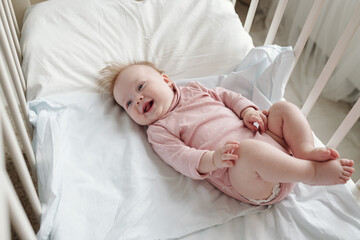 Wall Mural - Happy adorable baby in pink clothes having fun while lying in crib