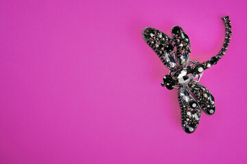 A thematic snapshot of fashionable jewelry accessories. An expensive and beautiful brooch in the form of a dragonfly, decorated with sparkling black stones-rhinestones on a purple background.Copyspacе