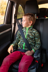 Little boy sitting on a booster seat buckled up in the car.