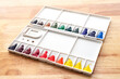 © Lifestyle Graphic - Watercolor paints set. Color in watercolor palette dirty on wooden background.