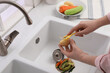Woman peeling potato over kitchen sink with garbage disposal at home, closeup