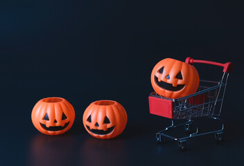 Halloween pumpkins on shopping cart  or trolley and on the floor on  black background with copy space. Halloween holiday concept.