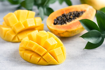 sweet ripe mango and papaya tropical fruit cut in half on grey concrete background closeup view