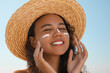 © New Africa - Beautiful African American woman with sun protection cream on face against blue sky
