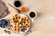 Sweet belgian waffles with blueberries, honey and cup of black coffee on a wooden table background, top view, copy space