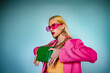 Fashion portrait of confident woman holding trendy green quilted leather bag with chunky chain. Model wearing pink sunglasses, blazer. Accessories advertising conception. Copy, empty space for text