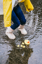 Crop Girl In Gumboots Jumping On Puddle With Splashing Water