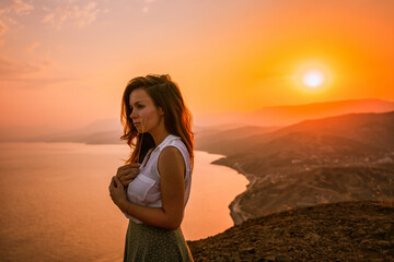 A beautiful woman standing and enjoying life at sunset in the mountains above the sea in the Crimea