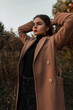© alones - Young beautiful girl with red lips in a fashionable coat with a sweater posing outdoors in the forest