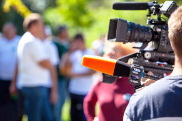 Wall Mural - Microphone in focus at media interview or event, blurred television camera and people in the background