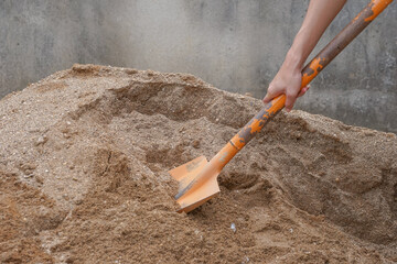 pile of sand, hand of a construction worker scooping sand for mix mortar on construction site, selective focus.