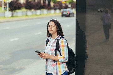 Young woman trying to catch a taxi at a bus stop using an app from a mobile phone