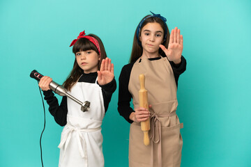 Canvas Print - Little sisters cooking at home isolated on blue background making stop gesture denying a situation that thinks wrong