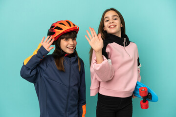 Wall Mural - Little sisters practicing cycling and skater isolated on blue background saluting with hand with happy expression