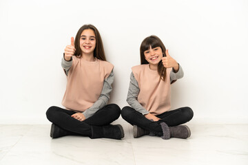 Wall Mural - Little sisters sitting on the floor isolated on white background giving a thumbs up gesture because something good has happened