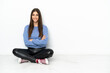 © luismolinero - Young woman sitting on the floor isolated on white background smiling a lot