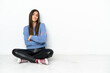 © luismolinero - Young woman sitting on the floor isolated on white background making doubts gesture while lifting the shoulders