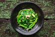 stir fried collards with salted fish and garlic in black ceramic plate on green old wood texture background, top view, collard greens