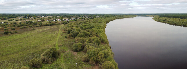  Beautiful aerial panorama of a Russian village near a wide river. Autumn rural landscape.