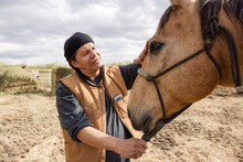 Male Farmer Petting Horse In Sunny Rural Paddock